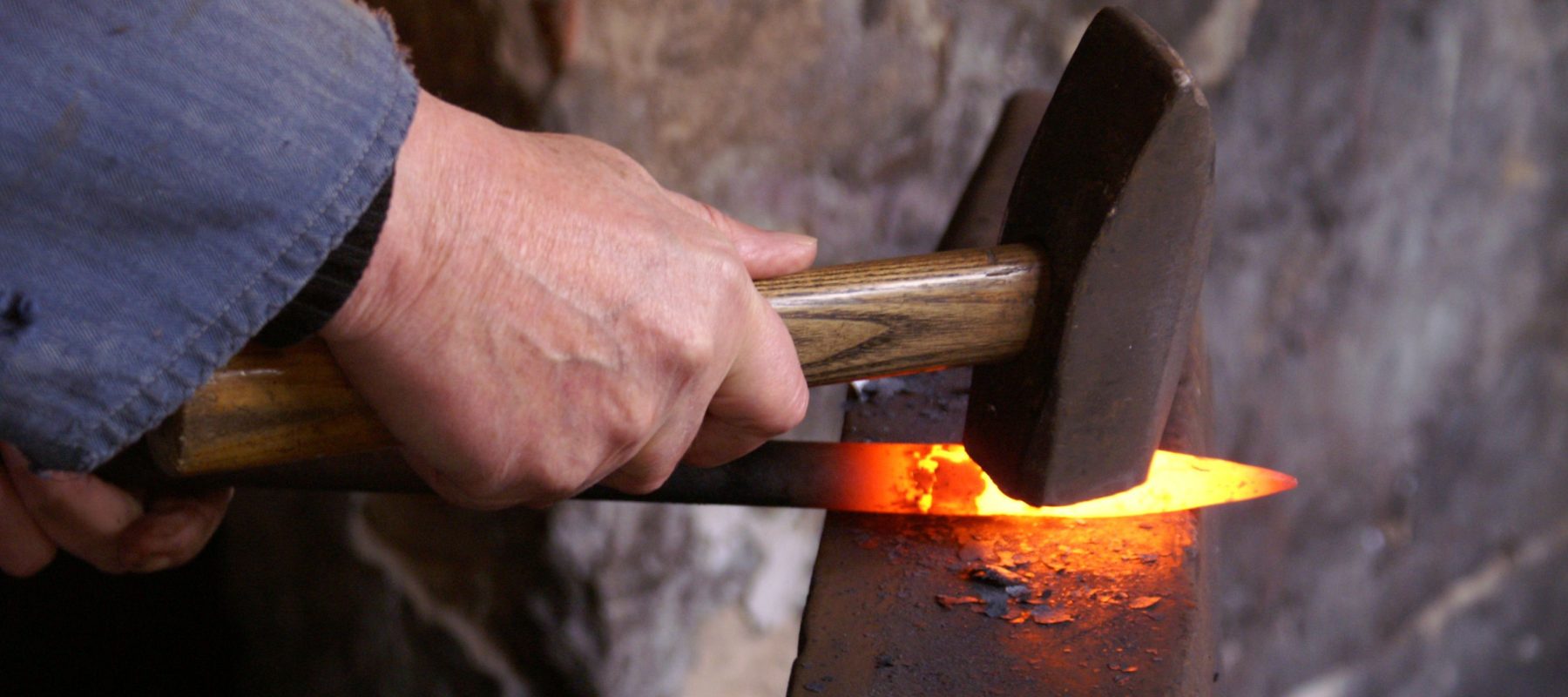 Hand mit Hammer über glühendem Eisen auf dem Amboss